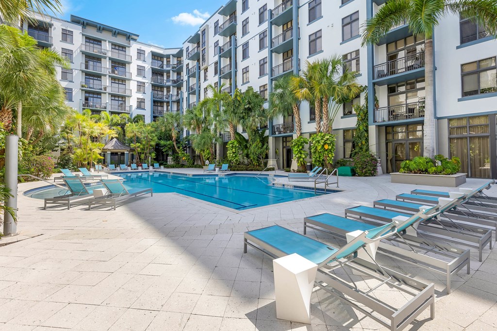 a swimming pool with chaise lounge chairs in front of an apartment building