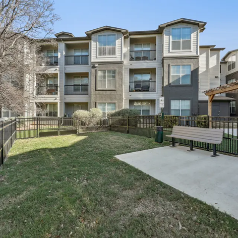 Apartment complex with a grassy area and a bench.