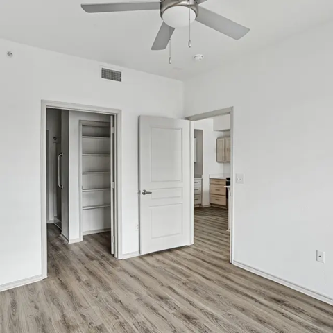 A room with a ceiling fan and a door to a refrigerator.