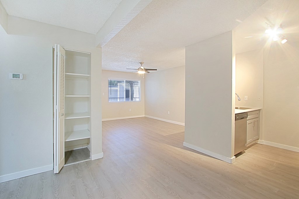 an empty living room with a kitchen in the background