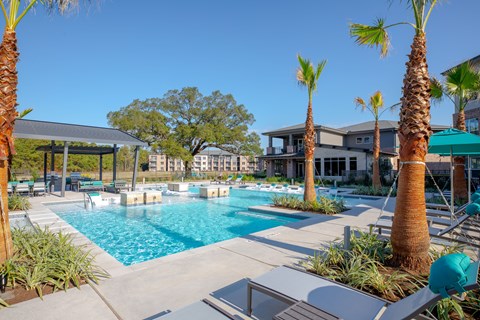 A pool surrounded by palm trees and a building in the background.