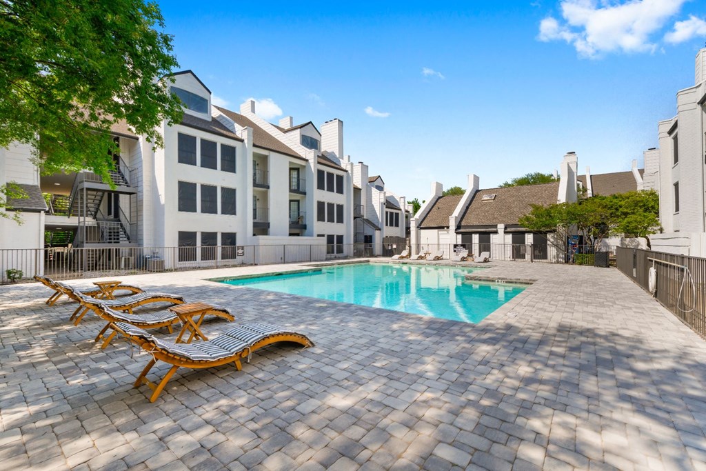 a swimming pool with chaise lounge chairs and buildings in the background