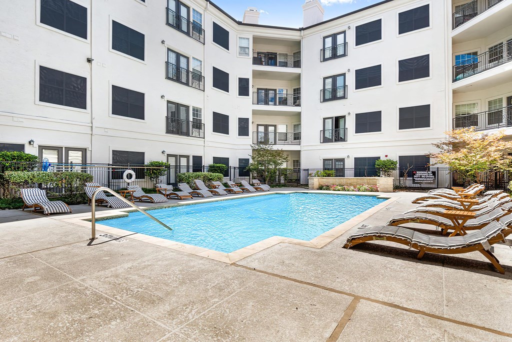 a swimming pool with chaise lounge chairs and an apartment building in the background