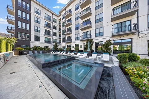 A large outdoor pool surrounded by lounge chairs and buildings.
