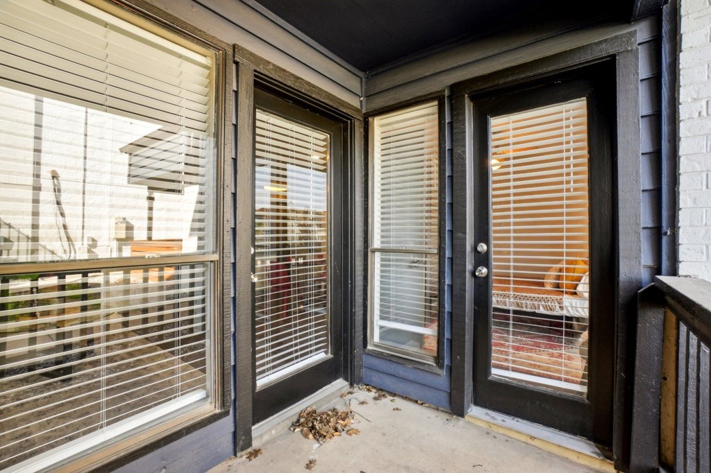 A balcony with a black door and a window with blinds.