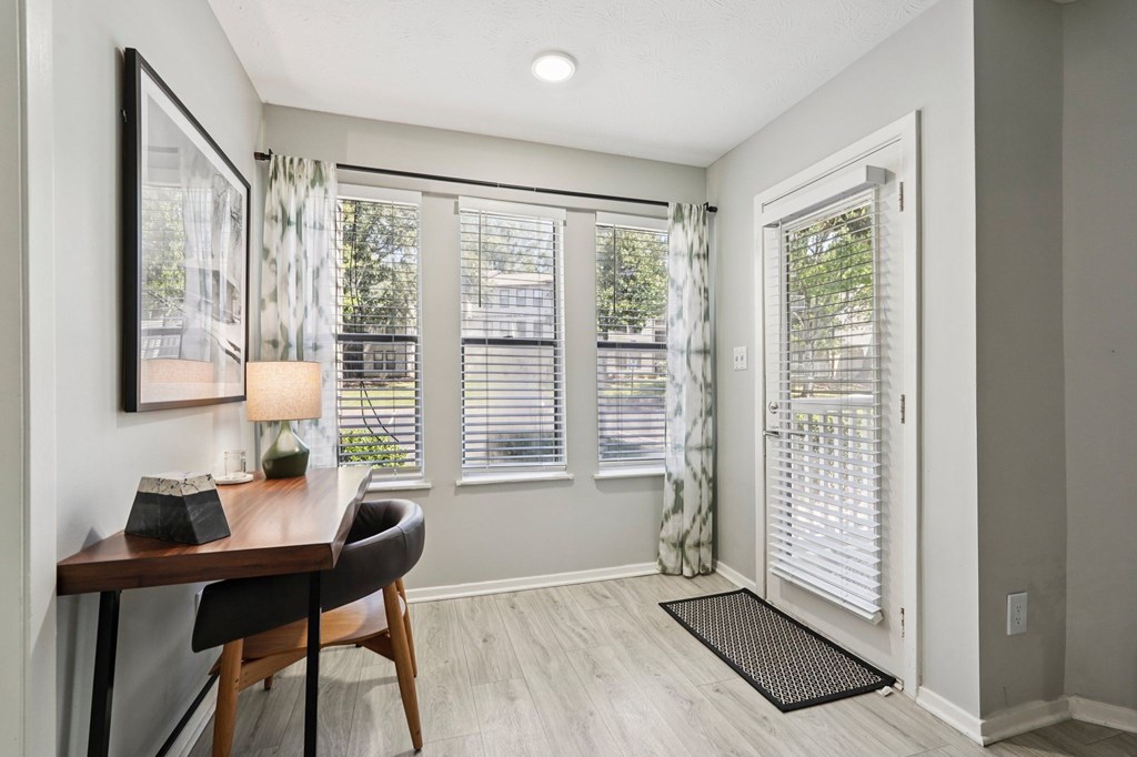 A room with a desk and chair in front of a window with blinds.