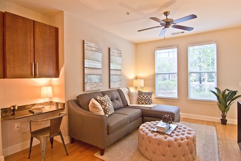 A living room with a grey couch and a round ottoman.