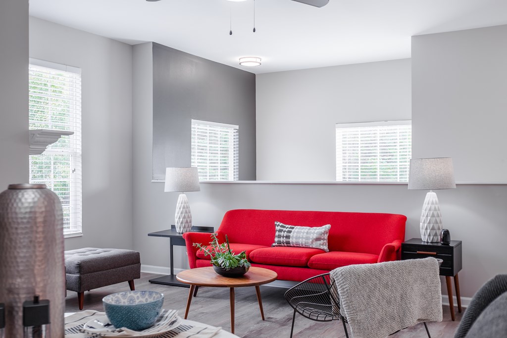 A living room with a red couch and a table with a plant on it.