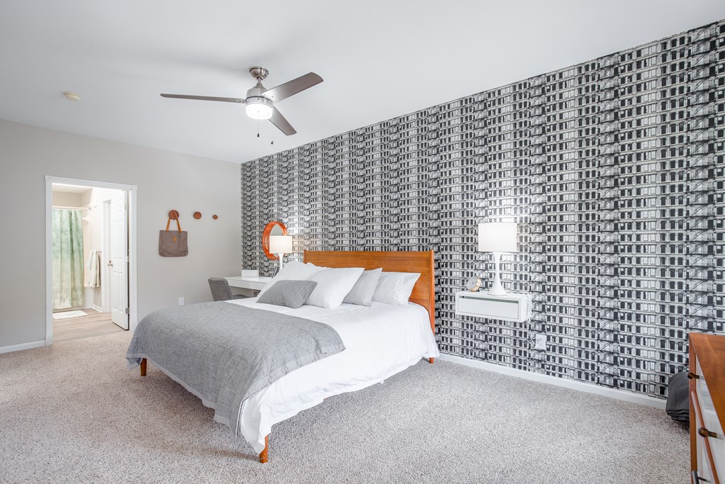 A bedroom with a bed, a ceiling fan, and a wall covered in black and white tiles.
