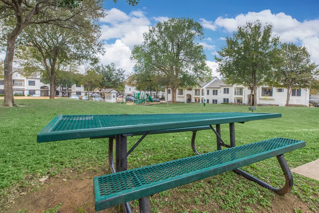 a green ping pong table in a park with a playground in the background