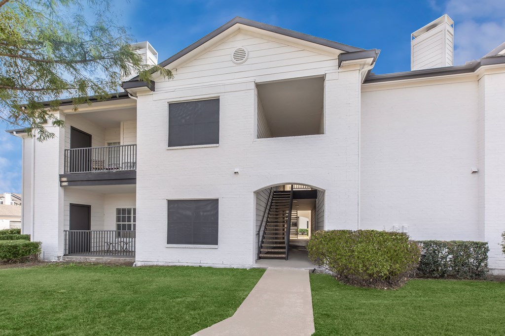 the outlook of a white building with a sidewalk and grass