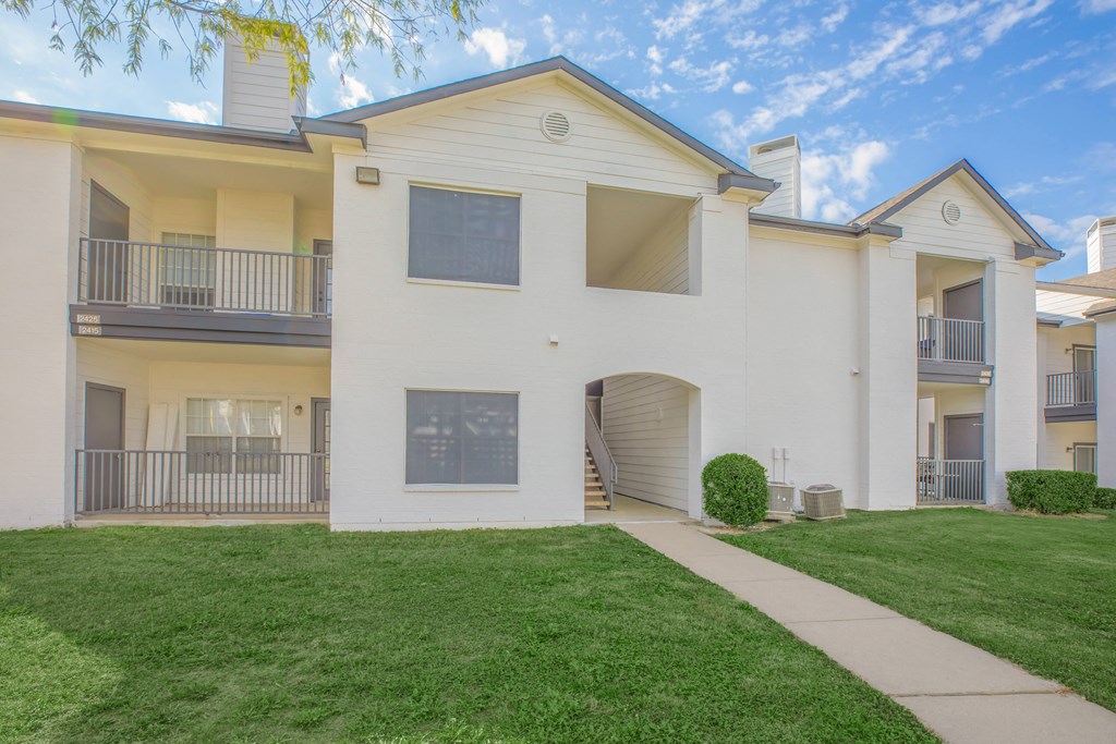 a white apartment building with a green lawn and a sidewalk