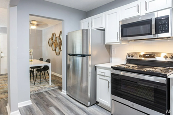 Kitchen with stainless steel appliances and white cabinetry with dining area in the background. - Photo Gallery 5