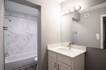 Bathroom with large mirror, sink, and tub/shower in the background. - Photo Gallery 7