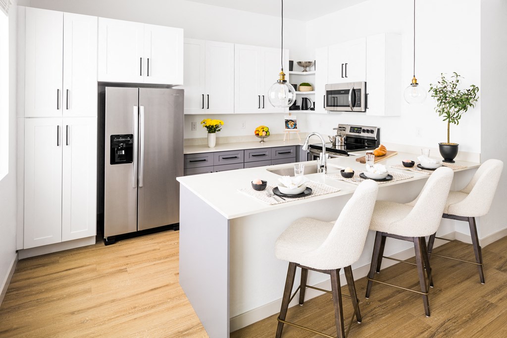 a kitchen with white cabinets and a white island with three white chairs