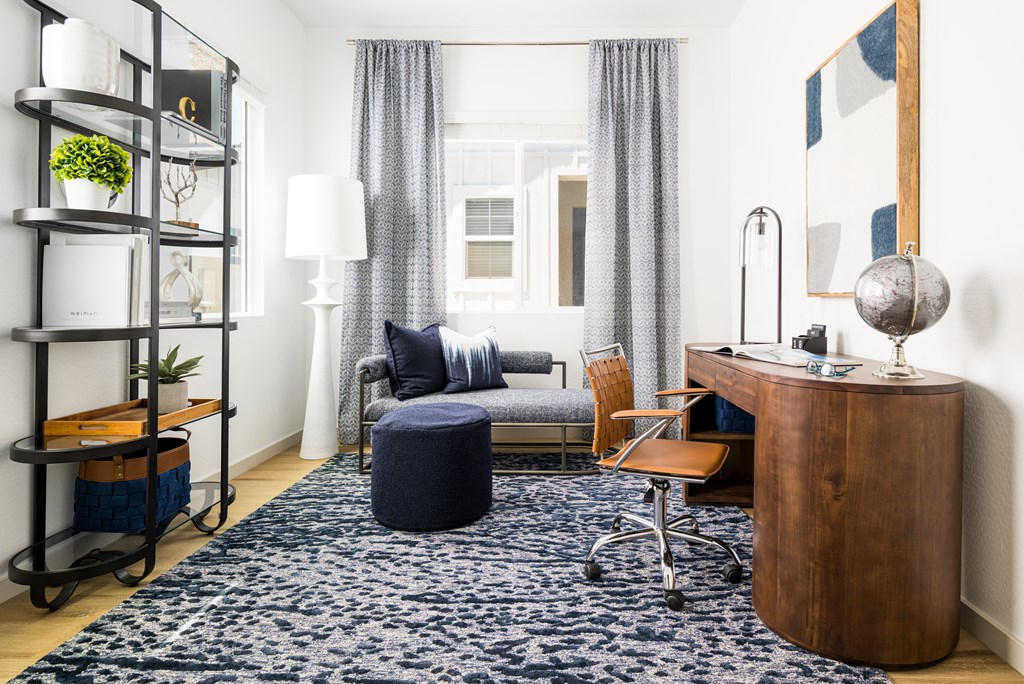 a living room with a blue rug and a desk with a chair and a couch in the