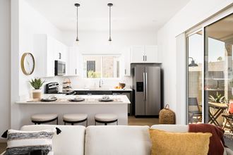 a kitchen and living room with a refrigerator and a counter with stools