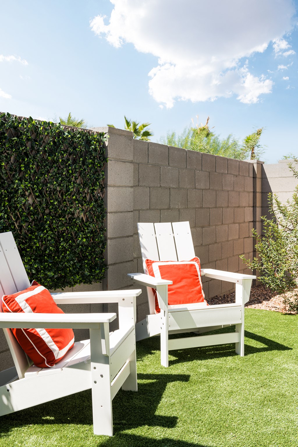 a backyard with white chairs and orange pillows and a privacy fence