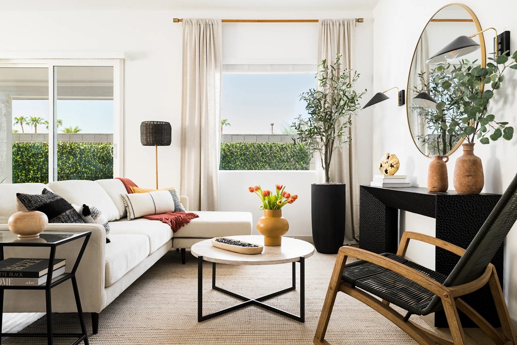 A living room with a white sofa, a coffee table, a chair, and a round mirror on the wall.