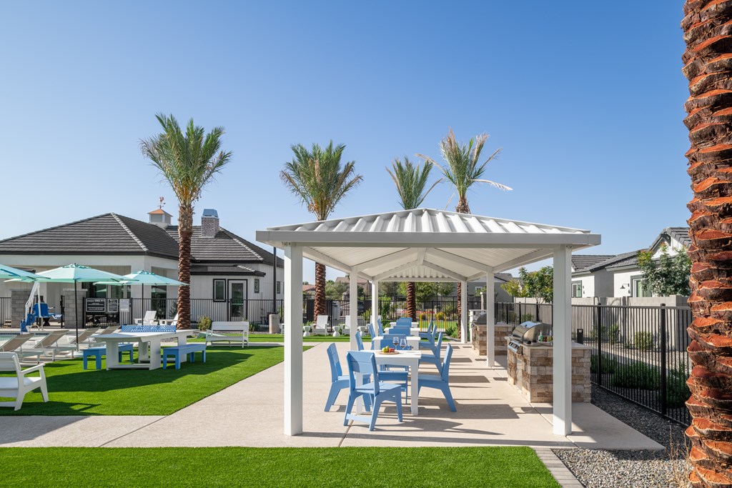 A white gazebo with blue chairs is surrounded by a lawn and palm trees.