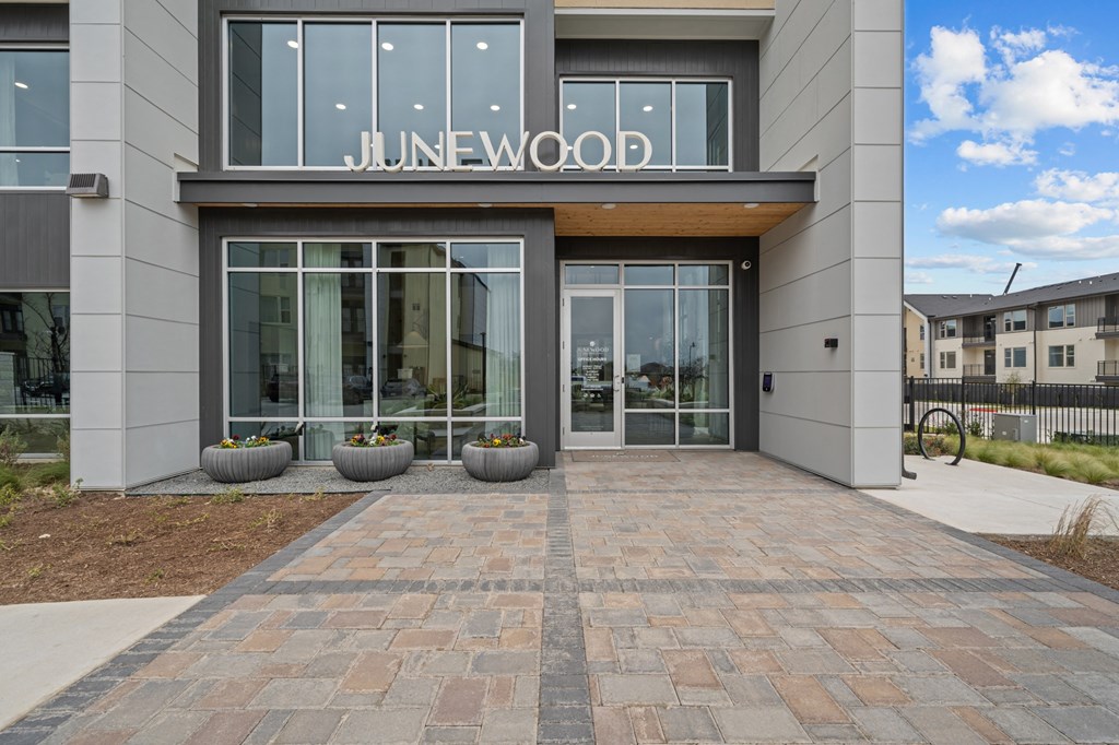 The image shows the front of a building named Junewood with a glass entrance and a brick walkway leading to it.