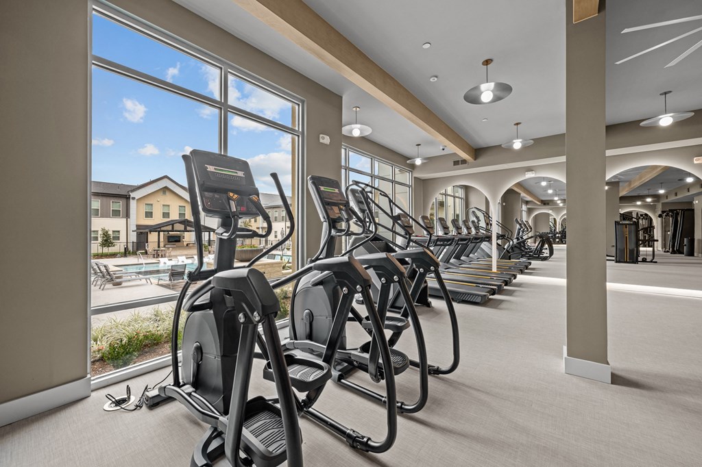 A gym with treadmills and a view of a residential area outside the window.