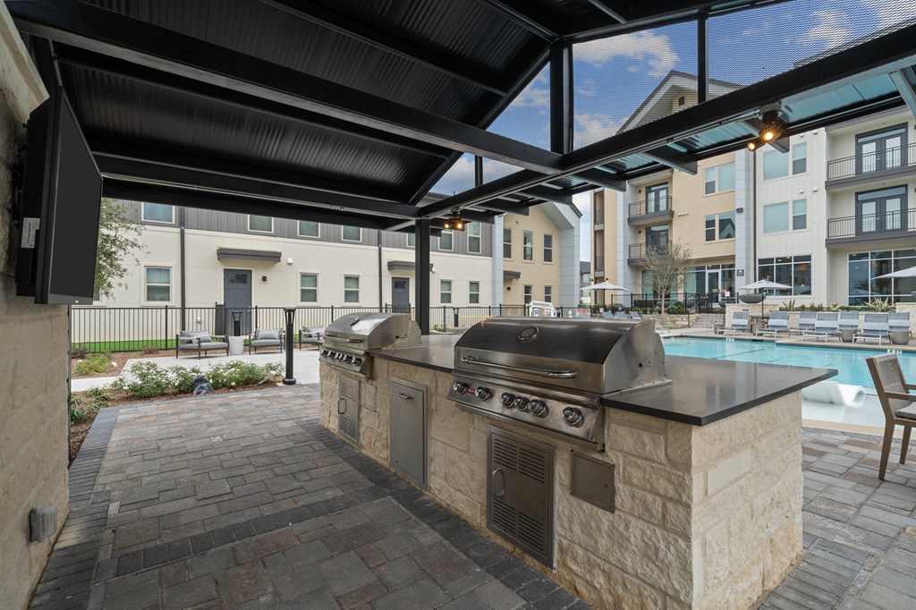 A patio with a grill and a pool in the background.