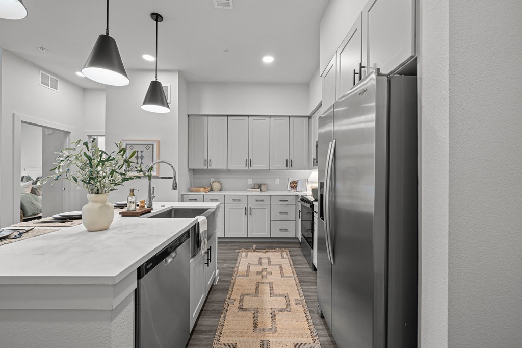 A modern kitchen with a refrigerator on the right and a countertop with a vase of flowers on it.