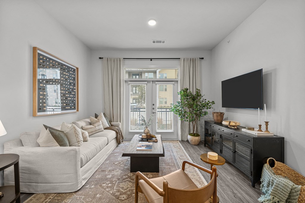 A living room with a white couch, a coffee table, a chair, a TV, and a plant.