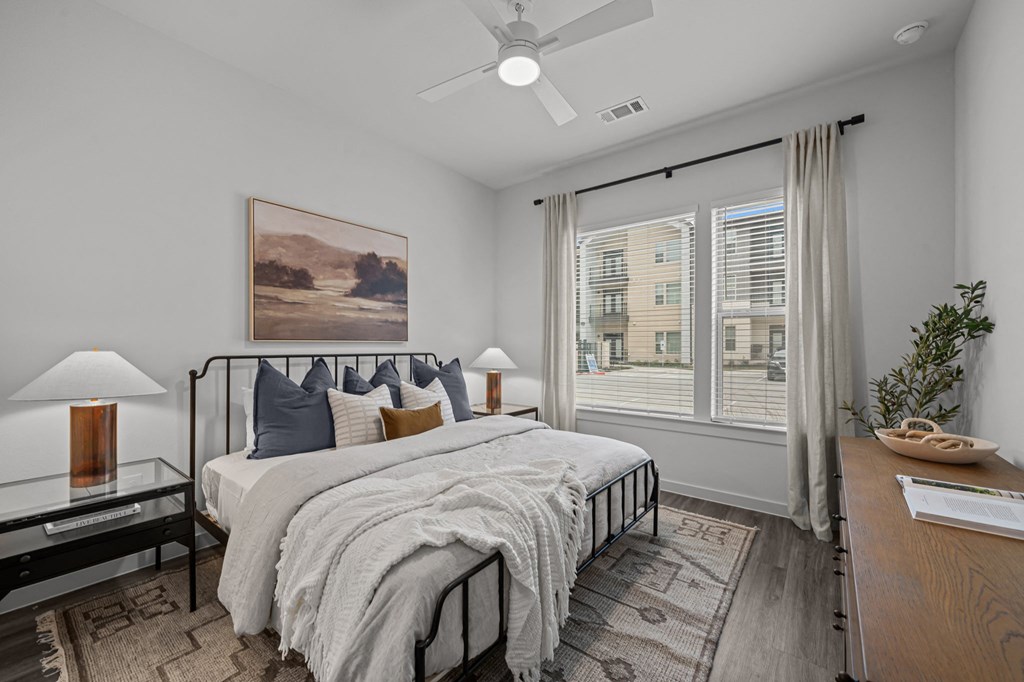A bedroom with a large bed, a ceiling fan, and a painting on the wall.
