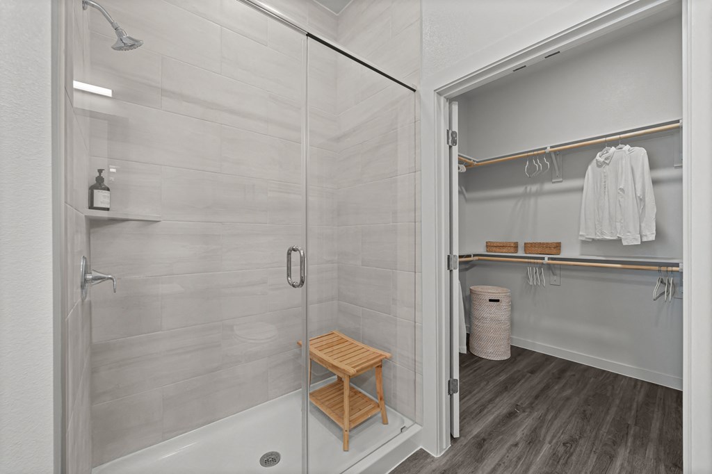A white bathroom with a walk in shower and a wooden stool.