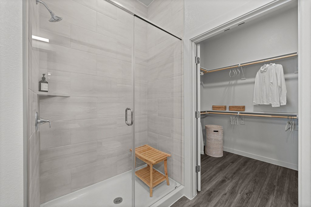 A white bathroom with a walk in shower and a wooden stool.