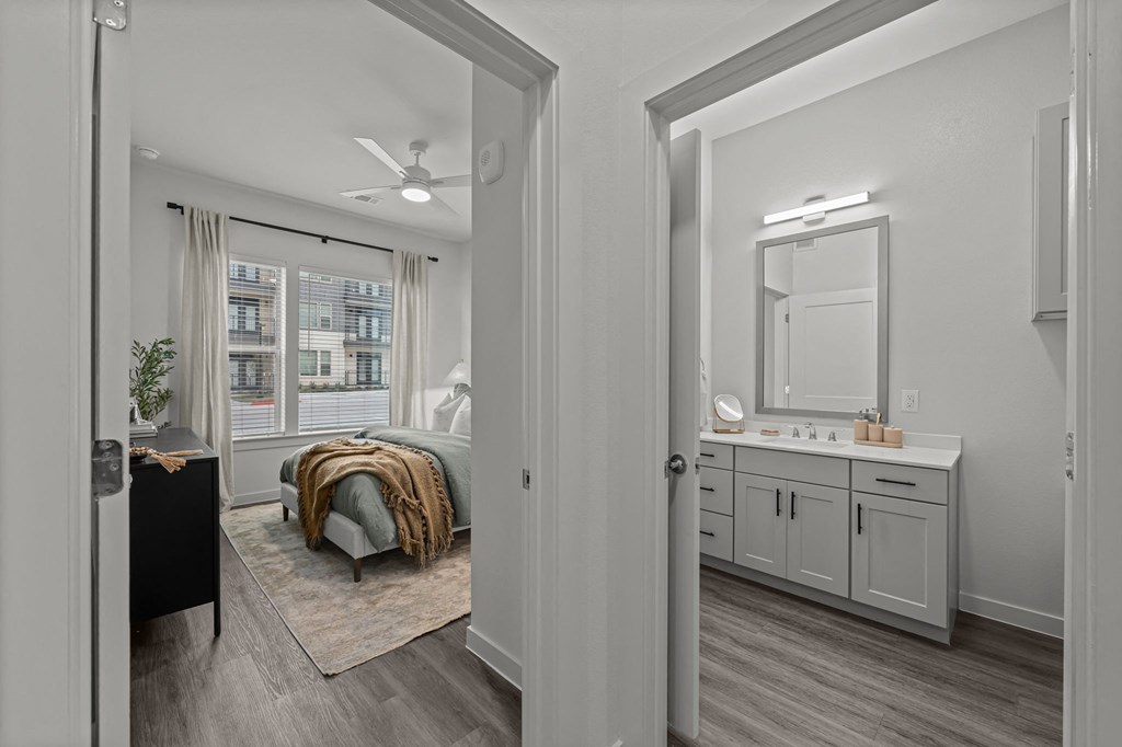 A bathroom with a vanity and a bedroom with a bed and a window.