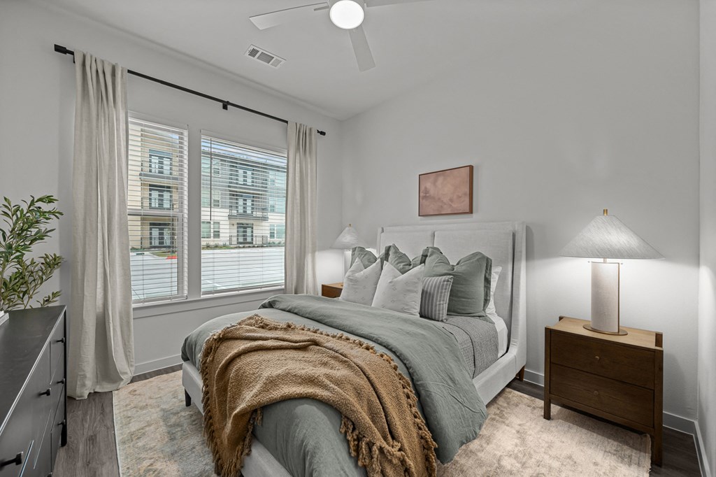 A bedroom with a bed, a nightstand, and a window with curtains.