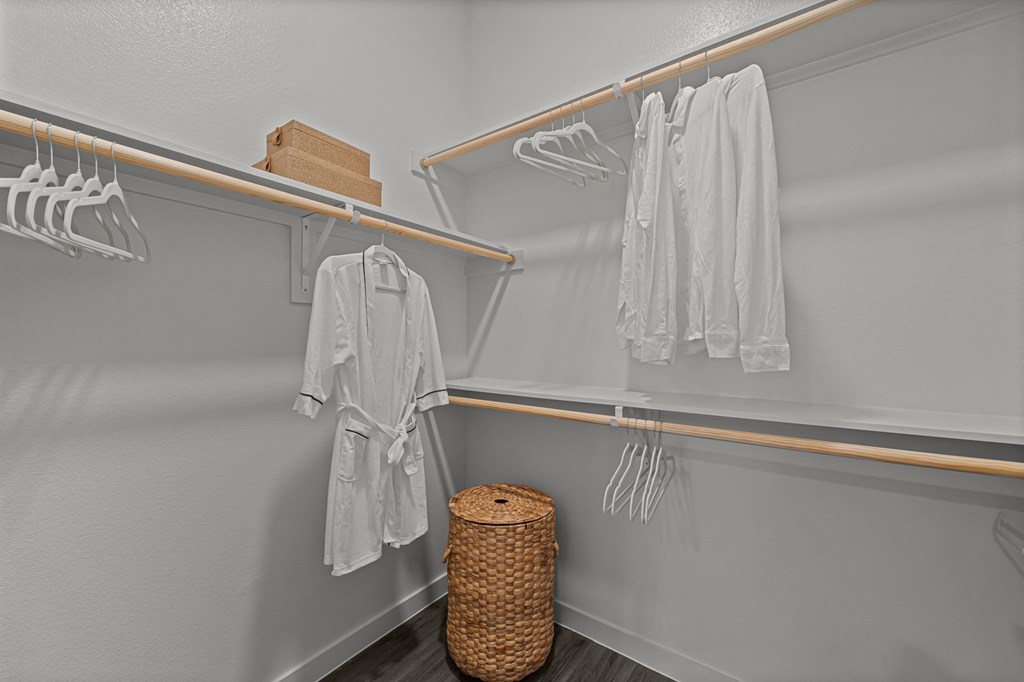 A white closet with clothes hanging and a basket on the floor.