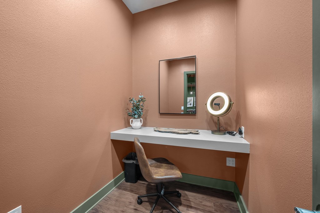A vanity table with a mirror, a plant, and a fan on a pink wall.