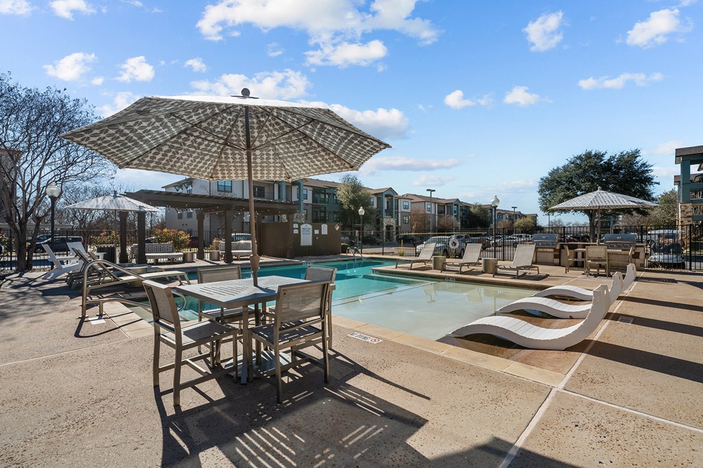 A sunny day at the pool with chairs and an umbrella.