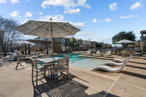 A sunny day at the pool with chairs and an umbrella.