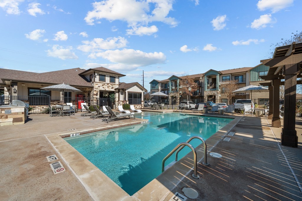 A large swimming pool surrounded by a patio area with chairs and umbrellas.