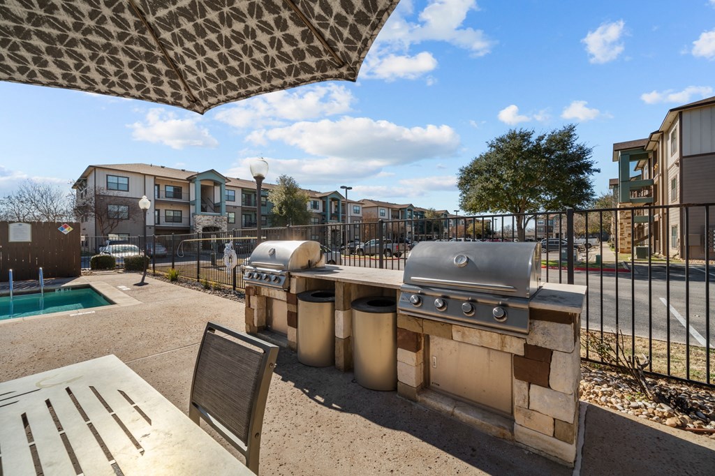 A patio with a grill and picnic table under a shade sail.