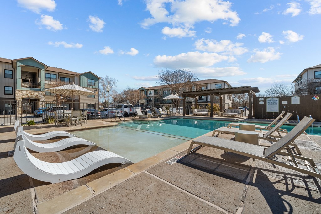 A pool area with sun loungers and a building in the background.