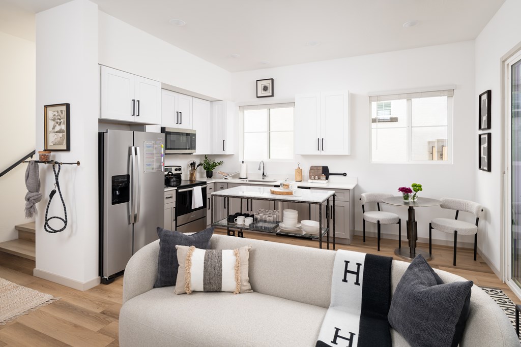 A modern kitchen with a refrigerator, a dining table with chairs, and a sofa with cushions.