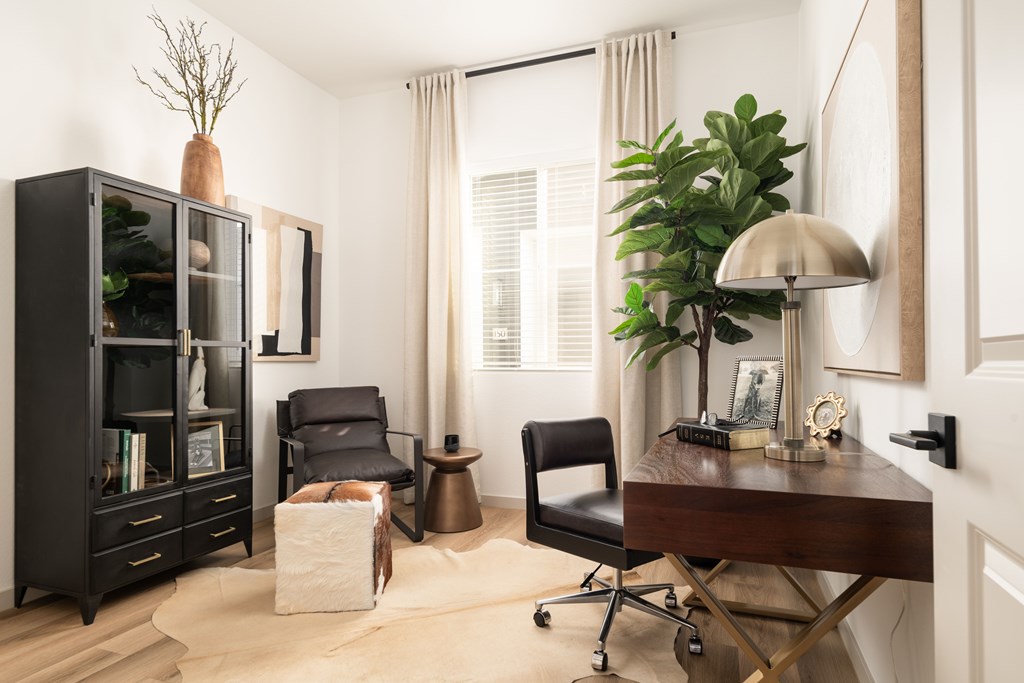 A black bookcase with a plant on top sits next to a desk with a lamp and chair.