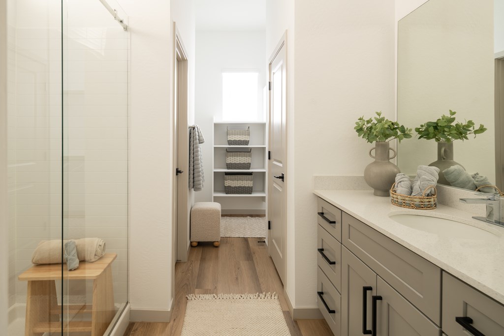 A bathroom with a glass shower door, a wooden stool, a sink, and a mirror.