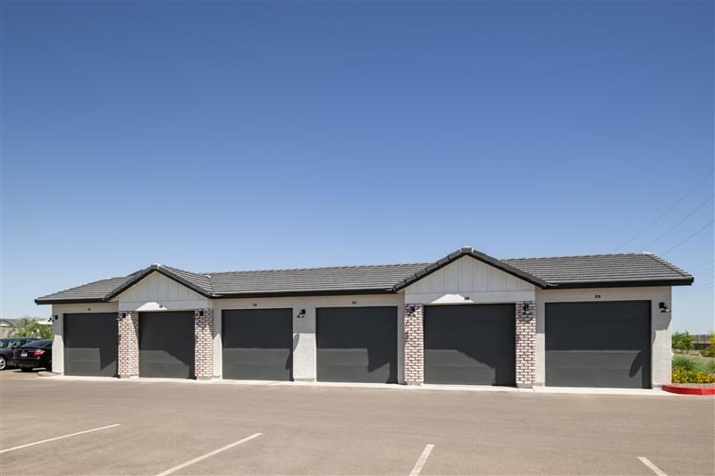 A building with a black roof and grey walls with a parking lot in front.
