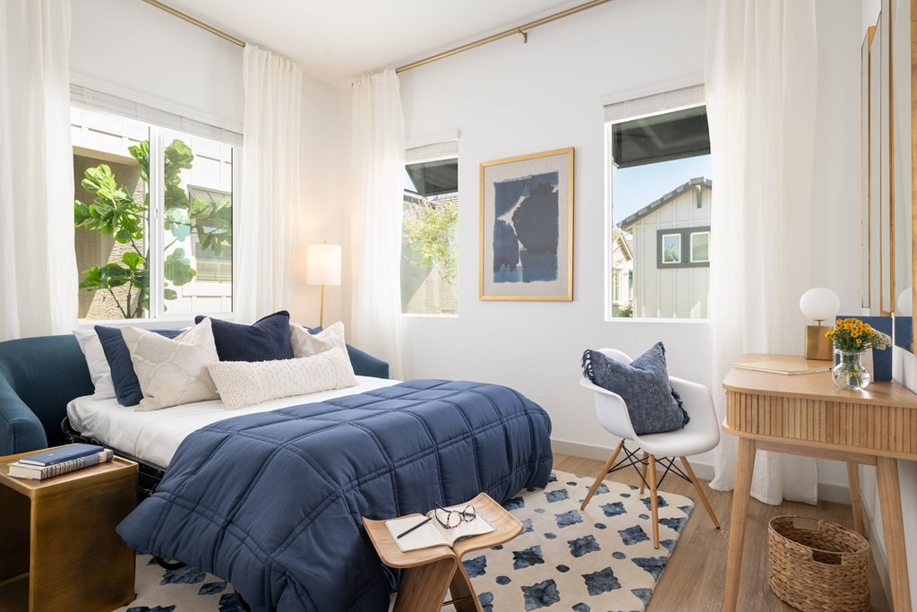A bedroom with a bed covered in a blue comforter and a white chair.