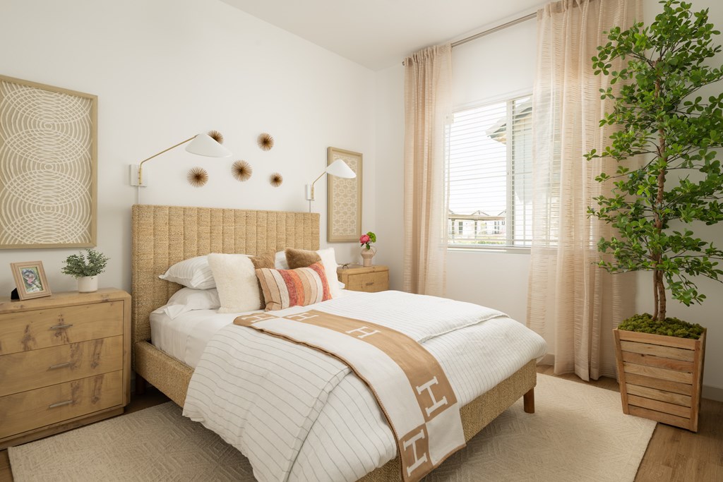 A bedroom with a bed, nightstand, and a plant.