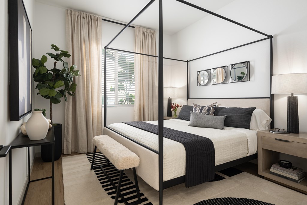 A modern bedroom with a four poster bed and a plant on the side table.