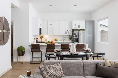 A modern living room with a grey couch and a kitchen in the background.