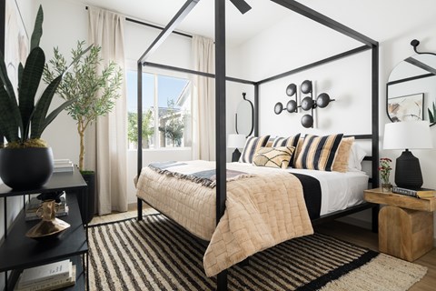 A bedroom with a four poster bed and a cactus on the side table.